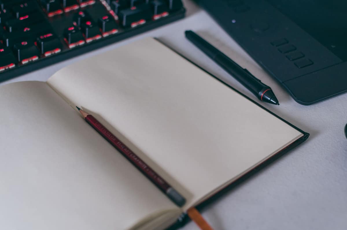 A small notebook open on a desk beside a pen