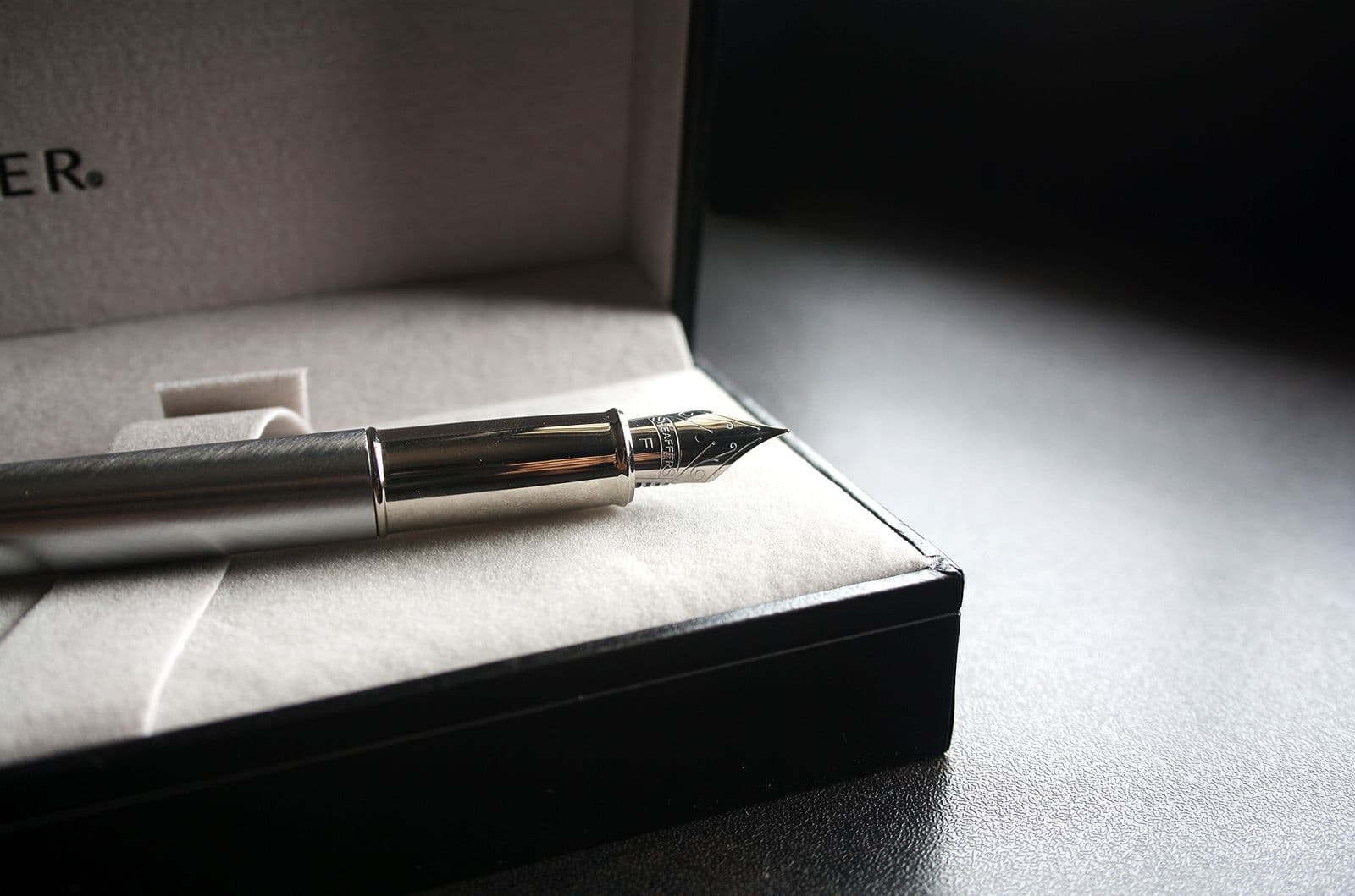 A silver fountain pen lying in an open velvet-lined presentation box