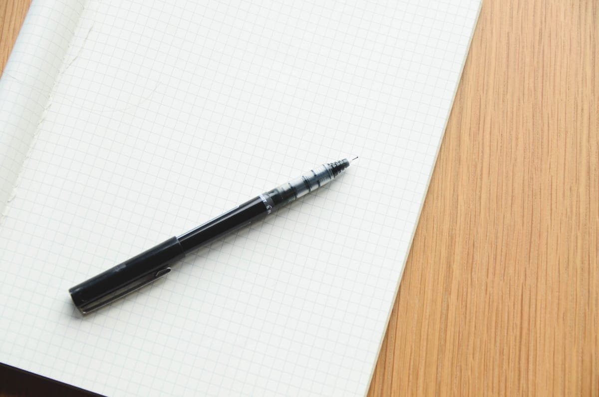 A bottle of black ink beside an open notebook on a desk