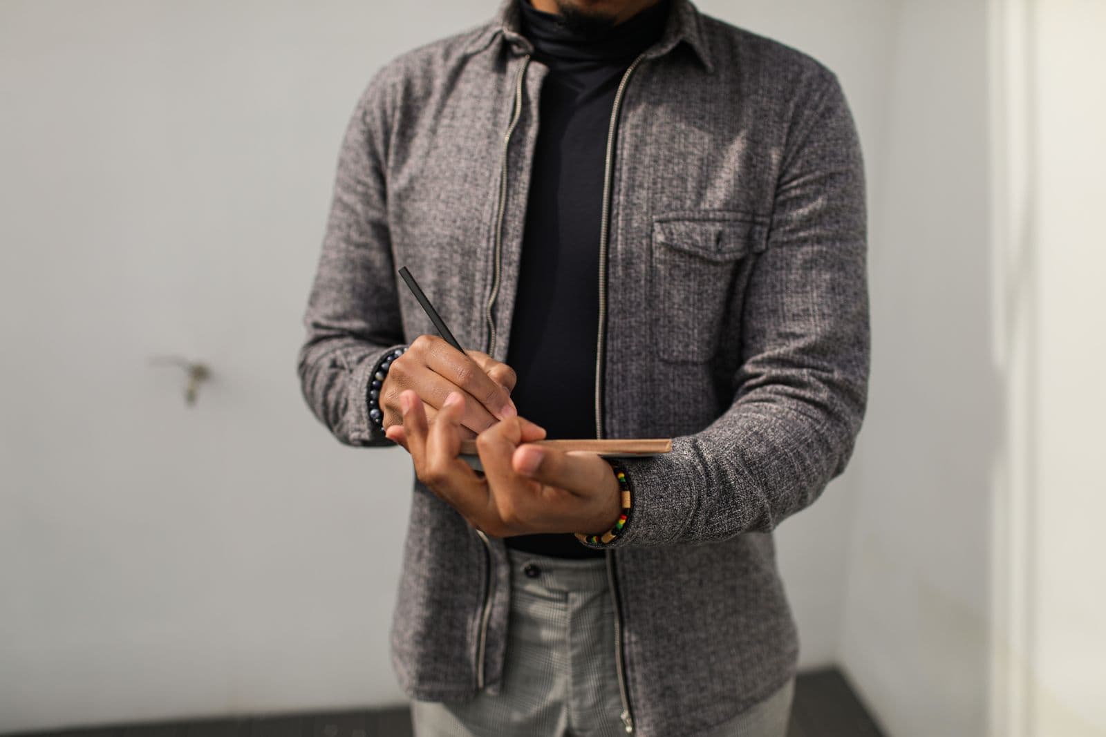A person in a gray jacket writing in a small notebook held in one hand