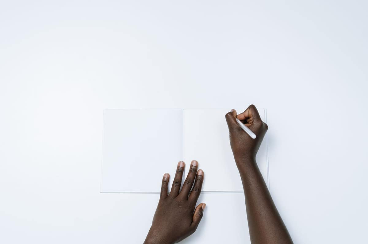 A person writing with their left hand in an open notebook