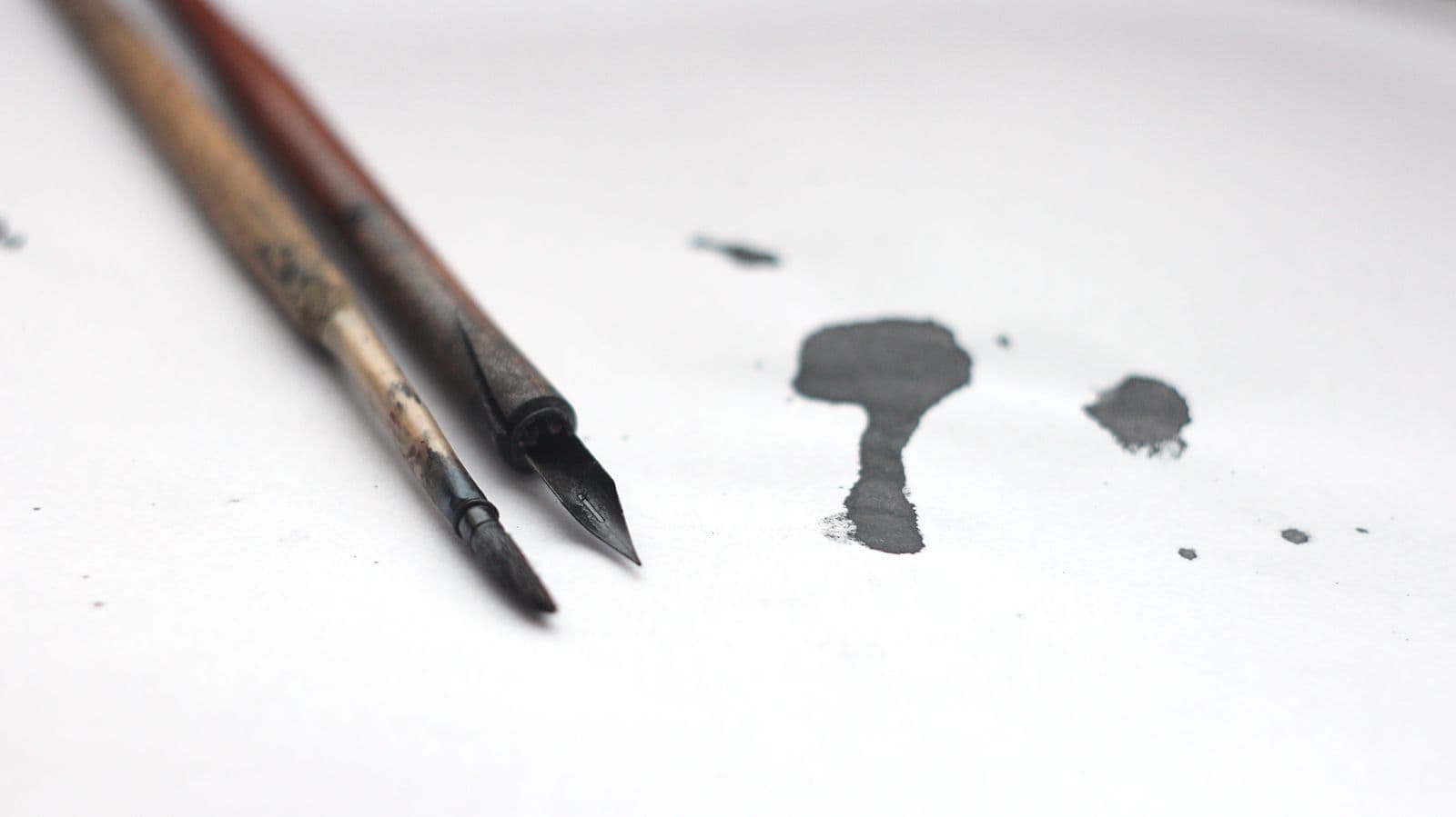 Close-up of calligraphy tools and spilled ink on a white surface
